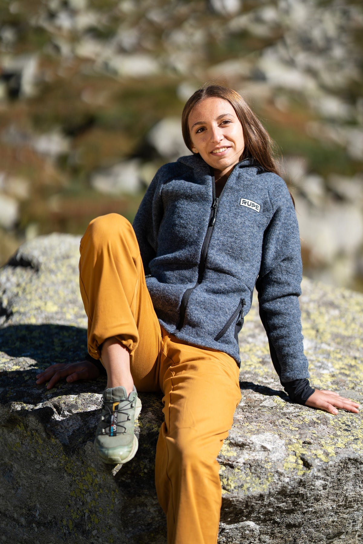 FW26-079 Peak Asfalt + Ande Ocra (donna seduta sul masso sorridente)